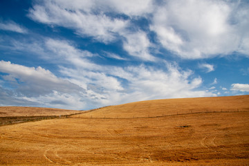 Harvested fields over rolling hills with clouds and blue sky