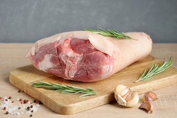 Uncooked pork knuckle on a wooden tray. Rosemary, garlic, salt and pepper for pickling shank. Light gray background. Close-up.