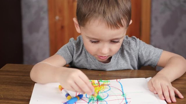 Unknown child draws with bright pencils while sitting at the table. Development and education of children of preschool age.