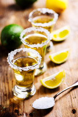 Golden mexican tequila in shot glass with lime and salt on vintage wooden table.
