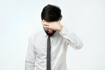 Feeling depressed. Exhausted young man covering face with hand while standing against grey background