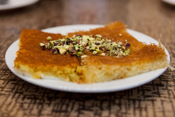 A plate of kunafah, a popular Arabian dessert, topped with chopped pistachio nuts in an Arabic bakery in Dubai, United Arab Emirates.