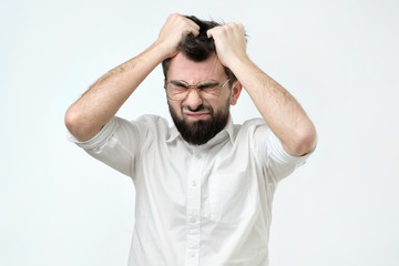 Enraged young businessman pulling his hair out for exasperation, having a burnout at work,...
