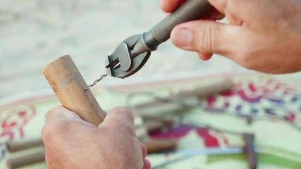 Senior man sits on the beach and making flute by hands, close-up.