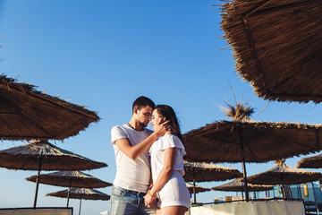 young couple in love hugging among reed umbrellas on the sea beach.