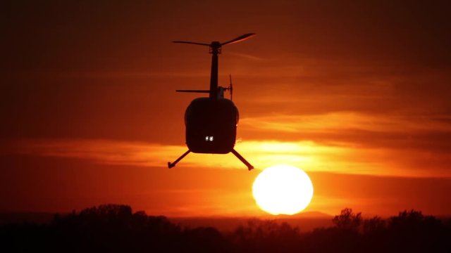 Helicopter on sunset background. Silhouette of a helicopter on a background of bright sun at sunset. Blockbuster shot. Helicopter against the red sky.