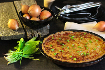 freshly baked onion cake in rustic style. in the background of the bow head on a wooden background. there is a bunch of greenery