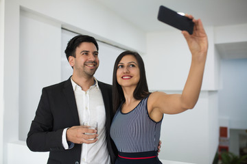 Cheerful young business couple taking selfie in office. Jolly mixed race colleagues photographing on smartphone. Business friends concept