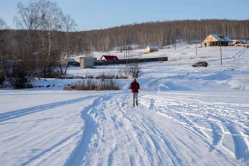 The girl runs away over the frozen lake in the direction of the village on a hill, on a winter sunny day.