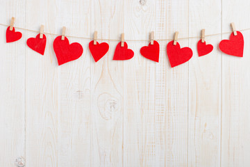 Red hearts on a rope with clothespins, on a white wooden background. Place for text, copy space.