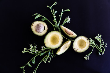 sliced avocado and flowers on black background