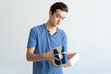 Serious teen boy holding open gift box. Young man standing and looking into gift box. Gift concept. Isolated view on white background.