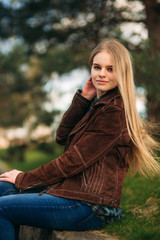 Obraz premium Attrective young girl sits by the embankment. Blond hair and brown jacket. Spring