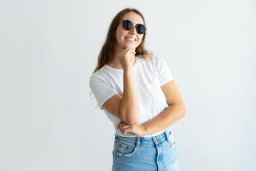 Fototapeta premium Smiling young woman wearing sunglasses and posing at camera. Girl touching chin and looking at camera. Young woman concept. Isolated front view on white background.