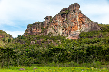 Obraz na płótnie Canvas Rock formation with cliffs known as Serra da Pedra da Águia, forest, grassy field and cloudy sky, Urubici, Santa Catarina