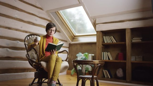 Woman reading book while drinking coffee on attic