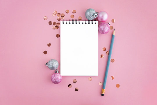 Clean notebook with pencil on pink background with confetti and christmas balls.
