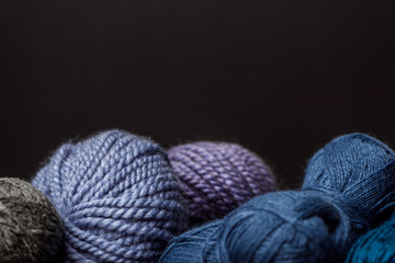 close up view of purple, blue and grey yarn balls on black backdrop