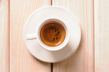 Black coffee in white cup and plate on bright wooden table