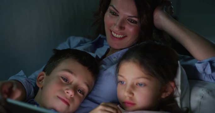 Portrait of happy mother and kids using a tablet on sofa in the evening in slow motion.