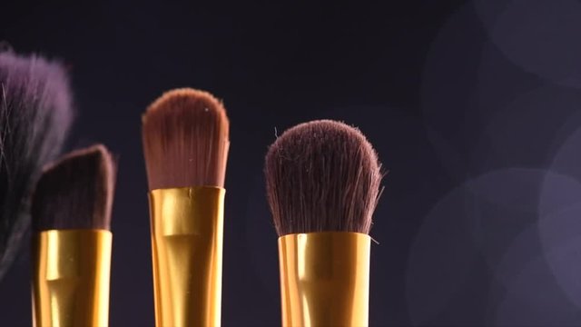 Makeup brushes set over black holiday blinking background. Various professional make up brush on dark backdrop in studio. Make-up artist tools. Dolly shot. Slow motion. 4K UHD video footage. 3840X2160