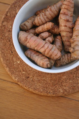Turmeric rhizome in a bowl on wooden table. Curcuma longa with selective focus
