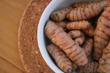Turmeric rhizome in a bowl on wooden table. Curcuma longa with selective focus
