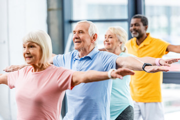 happy multicultural senior athletes synchronous doing exercise at gym