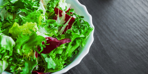 various fresh mix salad leaves with lettuce, radicchio, and rocket in bowl on dark wooden background