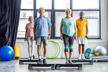 multiethnic senior athletes synchronous exercising on step platforms at gym