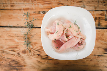 Fresh organic chicken meat on white dish with rosemary on the wooden table