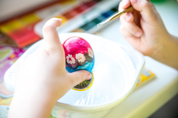 little girl paints an Easter egg with bright colors