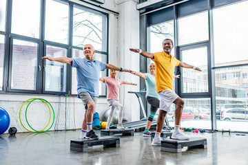 joyful senior multicultural athletes synchronous exercising on step platforms at gym