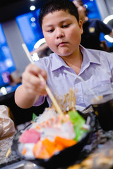 Asian boy is using chopsticks to chop mixed Sashimi on ice with selective focus