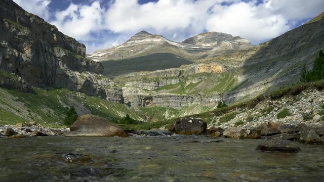 Monte Perdido mountain massif in Pyrenees near the border with France in Aragon, Spain. A panorama of a waterfall (top of it) waters, a green valley, the mountains and a blue cloudy skies in Ordesa y