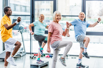 selective focus of multiethnic senior athletes synchronous exercising on step platforms at gym