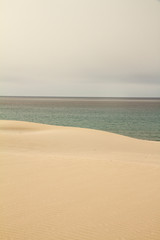 The gray sky breaks abruptly on the winter sea harmoniously marked by the yellow sand dune