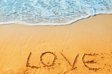 Valentine's Day concept, the word love writing on sand beach with blue waves ocean.