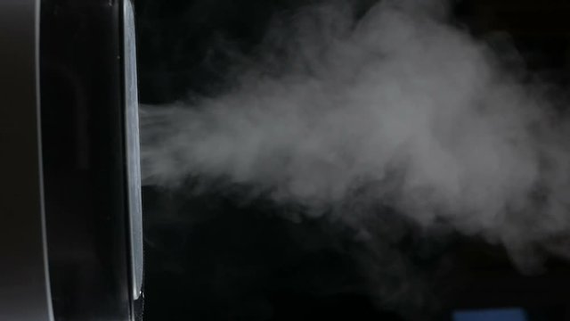 Mist from a black electric humidifier & oil diffuser in a dark room