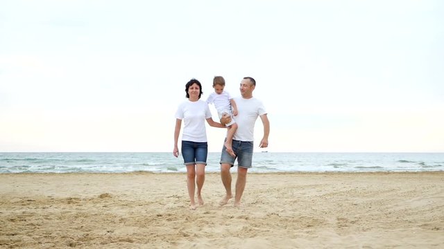 A happy family walks along the sandy beach on a sunny day. Recreation and tourism. People move towards the camera, leaving the focus.