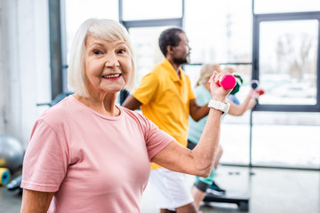 selective focus of cheerful senior woman and her friends exercising with dumbbells at gym