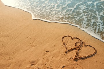 Valentine's Day concept, two heart shape writing on sand beach with blue waves ocean.