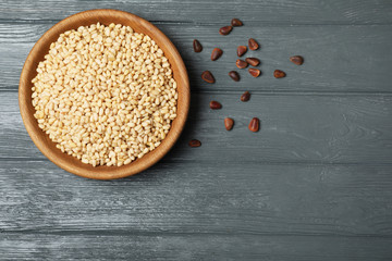 Dish with pine nuts on wooden background, top view. Space for text