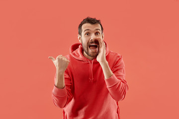 Wow. Attractive male half-length front portrait on coral studio backgroud. Young emotional surprised bearded man pointing to left. Human emotions, facial expression concept. Trendy colors