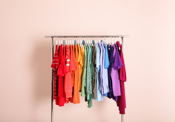 Wardrobe rack with different bright clothes on color background