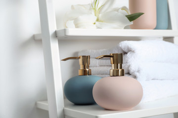 Fototapeta na wymiar Stylish soap dispensers and towels on shelf near light wall