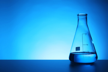 Conical flask with liquid on table against color background. Chemistry laboratory glassware
