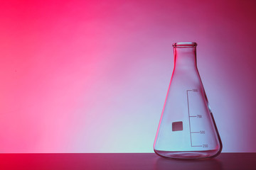 Empty conical flask on table against color background. Chemistry laboratory glassware