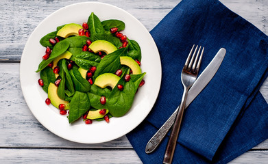 Avocado salad with baby spinach and pomegranate on a white plate on a wooden table