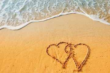 Valentine's Day concept, two heart shape writing on sand beach with blue waves ocean.